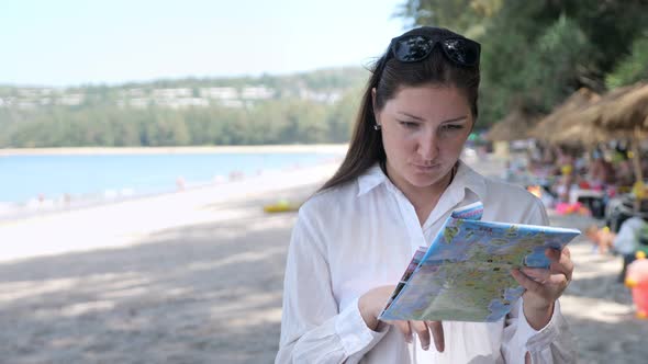 Young Woman in a White Shirt on the Beach Considers a Map