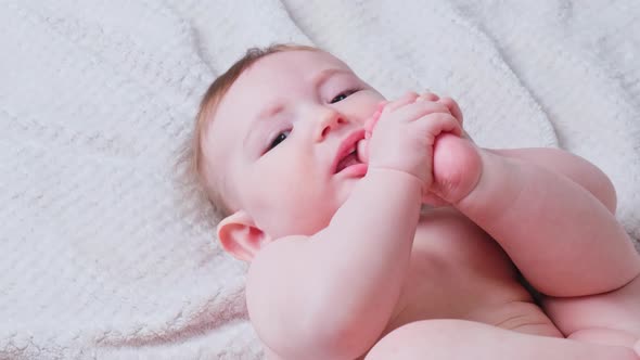 Portrait of a happy infant baby on the bed pulling his leg into his mouth, eight months old