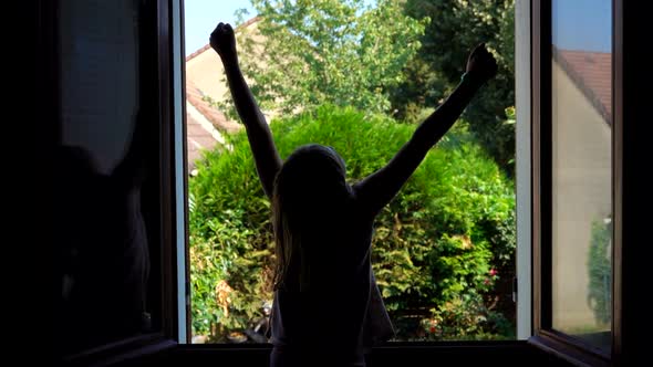 Silhouette of a Little Happy Girl Stretching Up on the Background of Open Window
