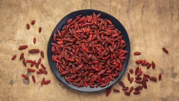 Dried goji berries are falling into black ceramic plate, stop motion animation