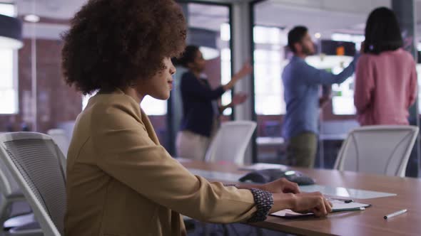 Mixed race businesswoman sitting smiling in meeting room with diverse colleagues in background