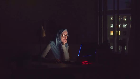 Muslim Girl with Glasses and a Hijab with Notebook in the Dark Search on the Internet at Home