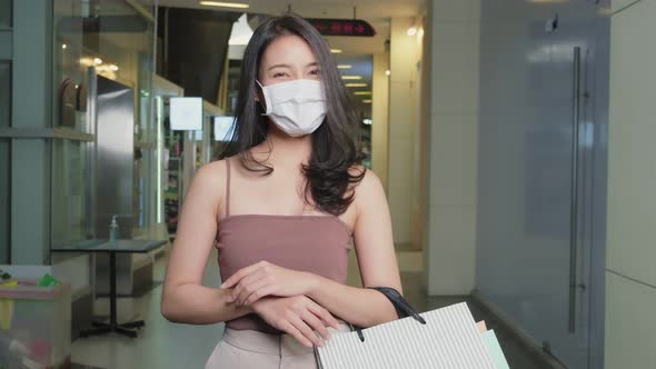 Portrait of Asian young woman wear mask, carrying shopping bags enjoy shopping in department store.