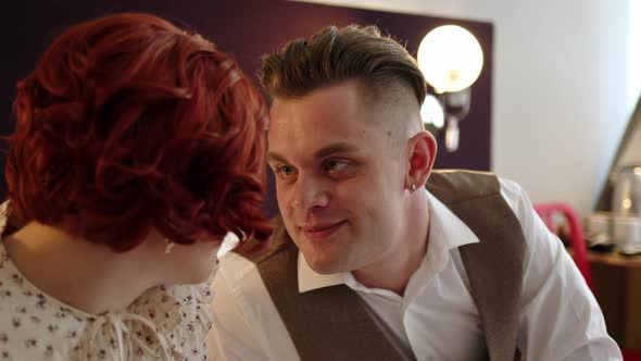 Couple of Man and Woman in Costumes Sit on Bed in Hotel or Apartment and Chat Looking Into Their