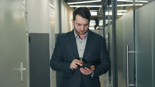 Young Businessman Uses a Mobile Phone to Work in the Office Corridor