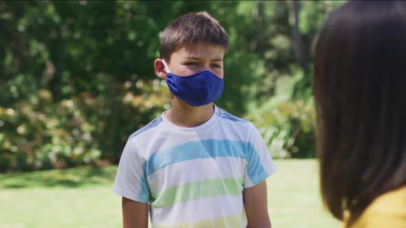 Portrait of caucasian brother and sister wearing face mask standing in the garden