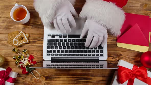 Top View Santa Hands are Typing on Keyboard Drinks Tea By Wooden Decorated Table