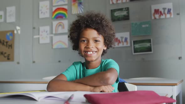 Video of happy biracial boy sitting at desk in classsroom