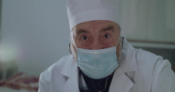 Portrait of Sad Older Doctor in Medical Mask Lightly Nodding Head at Camera