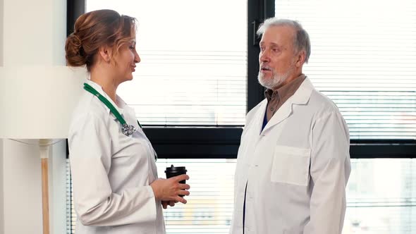 Woman Doctor and Mature Adult Physician Surgeon Having Conversation Drinking Coffee During Break