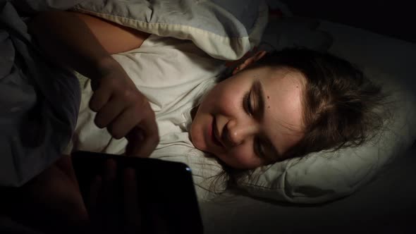 Little Girl Looking at The Smartphone And Then Hides Under The Blanket alt