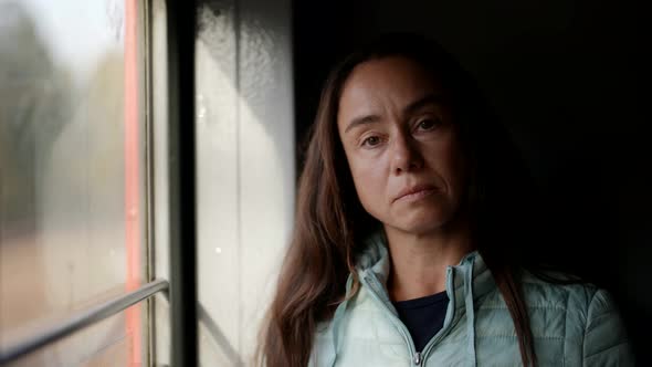 Pensive Middleaged Woman is Riding Train Standing Near Window Looking on Street