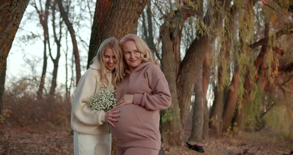 Pregnant Mother with Blonde Adult Daughter in Beige Clothes in Autumn Evening Park