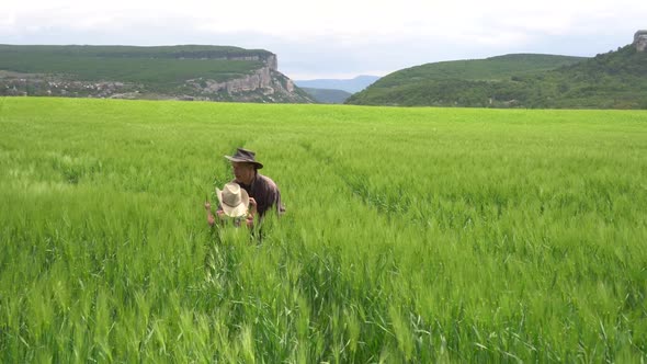 A Farmer Father with Happy Small Daughter Inspects a Green Wheat Field in Spring