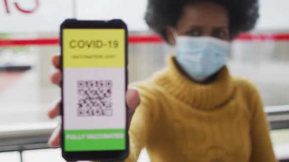 African american businesswoman with face mask preparing covid 19 certification on smartphone