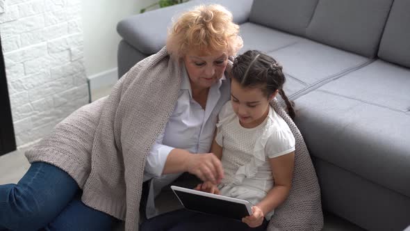 Smiling Grandmother and Granddaughter Waving By Hand and Having Video Call with Digital Tablet Home