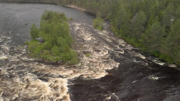 Aerial footage by drone of two men walking over small bridge over kalix rapid