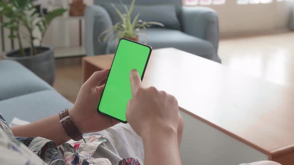 Man Sitting On Couch Using Smartphone With Green Screen Display