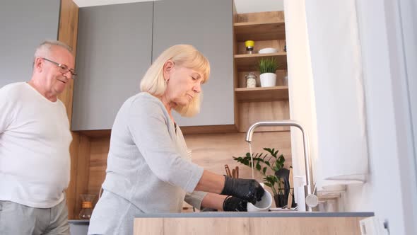 Old Blonde Woman Washing Dishes in Modern Kitchen in Sunlight