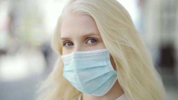 A Woman in a Medical Mask is Looking at the Camera and the Wind is Blowing Her Hair