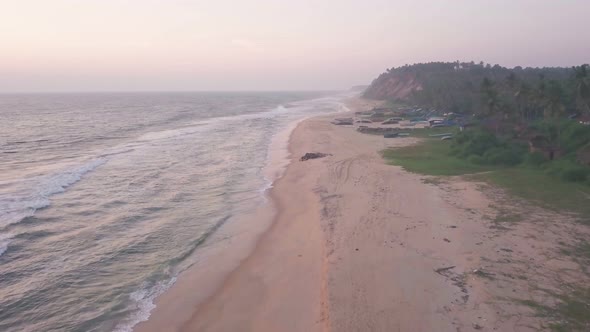 Aerial view of Varkala coastline with waves crashing on the sandy beach, in Kerala, India, at dusk