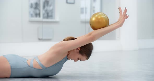 Woman Athlete Performs Callisthenics Exercises with Gymnastic Ball on the Floor at White Dance Hall