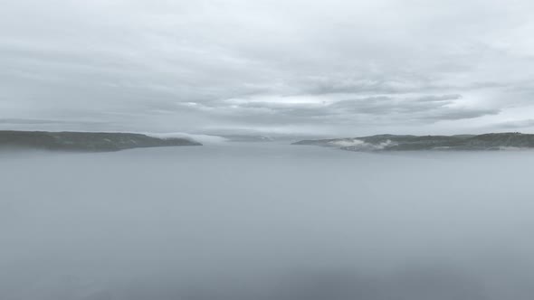 Aerial view over thick fog at the mouth of the river with black mountains in Quebec, Canada