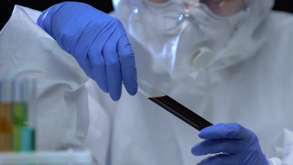 Chemist in Protective Uniform Showing Tube With Dark Liquid, Oil Examination