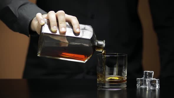 Pouring Whiskey, Cognac Into Glass with Ice Cubes. Bartender Pours Alcohol Drink