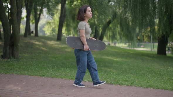Side View Young Caucasian Beautiful Woman with Dwarfism Strolling with Skateboard in Park