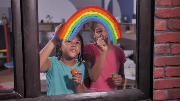 Cheerful Girls Painting Bright Rainbow on Window