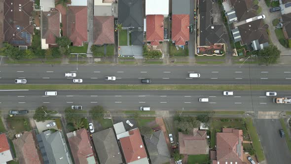 Aerial top down cars, buses, trucks, houses, properties on a main highway with two way traffic flowi