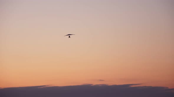 Dark Silhouette of Motorized Hang Glider with Passenger and Pilot, Flies, Soars in the Air, Against