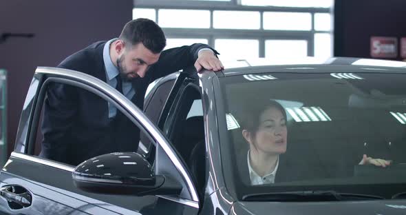 Portrait of Adult Successful Businesslady Sitting in Car and Consulting Dealer Standing Next To