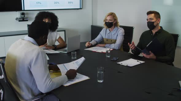 Diverse group of business colleagues wearing masks in discussion in meeting room