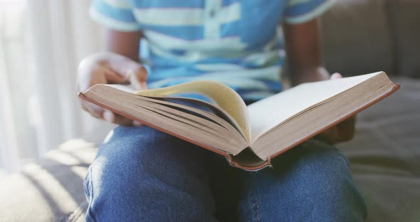 Mid section of african american boy reading a book sitting on the couch at home