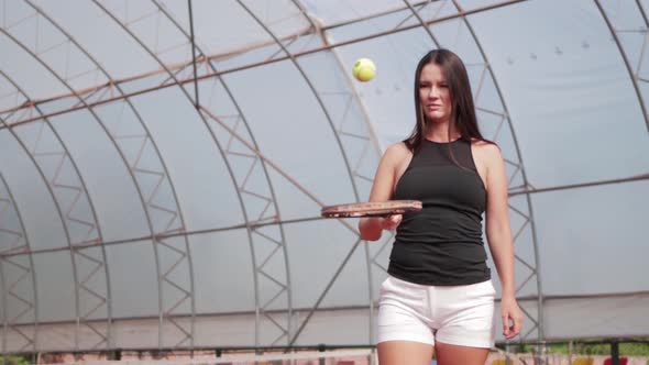 A Woman with Long Hair Beats a Tennis Ball From a Racket