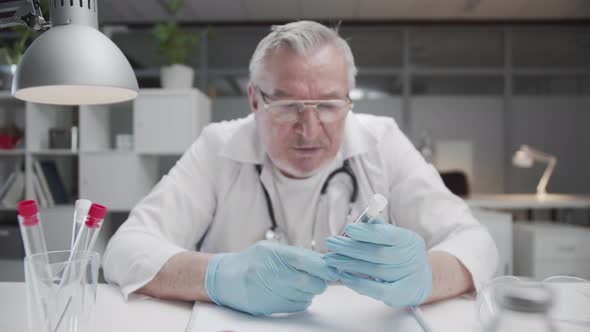 An Experienced Laboratory Assistant with Gray Hair Examines a Blood Sample of a Test Patient in a