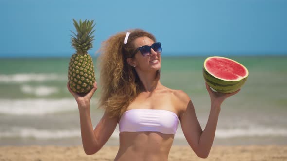 Young Beautiful Girl Has Fun at the Beach Near Sea Dancing with Tropical Fruit. Concept Joy and