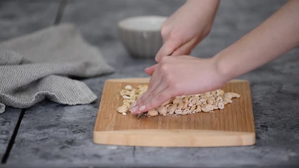 Closeup Womans Hands with Knife Cut Cashew Nuts on a Cutting Board in a Kitchen