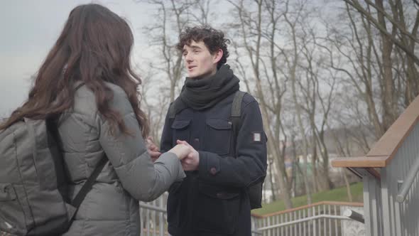 Portrait of Young Loving Caucasian Boy Holding Hands of Brunette Girl and Talking. Happy Guy with