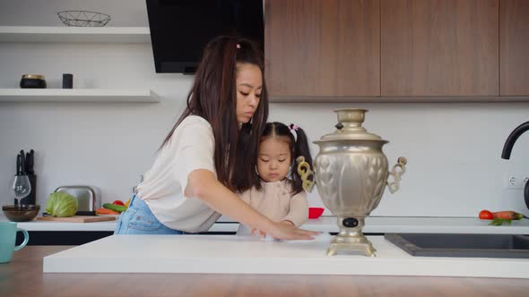 Asian Mom and Baby Daughter Cleaning Table in Kitchen