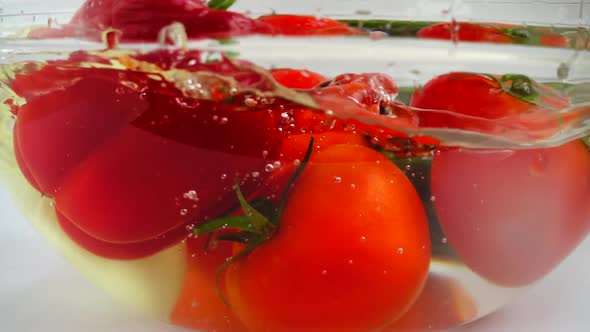 Tomatoes, onions, cucumber and red bell peppers in a glass bowl of water. Slow motion.