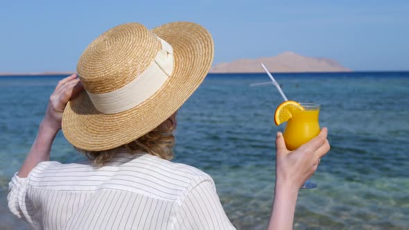 Woman In Straw Hat Holding Fresh Orange Juice At Beach On Vacation.