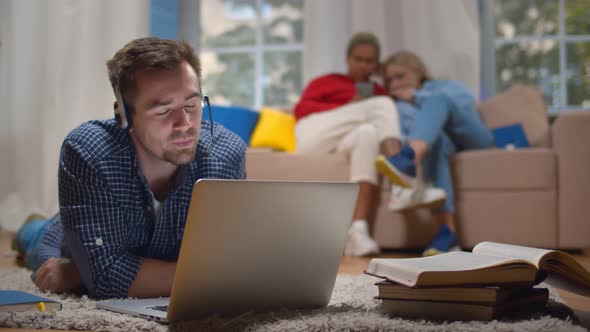 Young Man in Headset Having Educational Webinar on Laptop Studying on Floor in Dorm Living Room