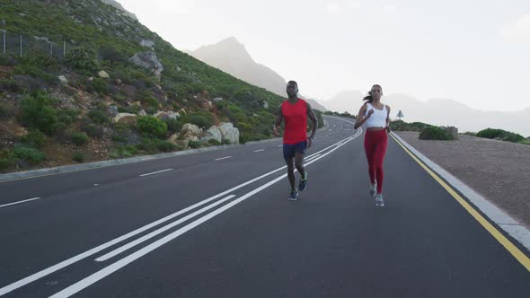 Diverse fit couple exercising running on a country road near mountains