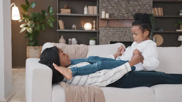 African American Loving Mother Mommy Lying on Sofa Relaxing at Home Living Room with Little Daughter