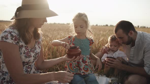 Young Happy Family with Children Resting on a Picnic in a Wheat Field and Eating Delicious Food