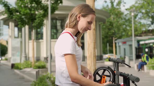 Woman Using Smartphone To Pay for Rental Electric Scooter While Standing on Parking Lot on Modern