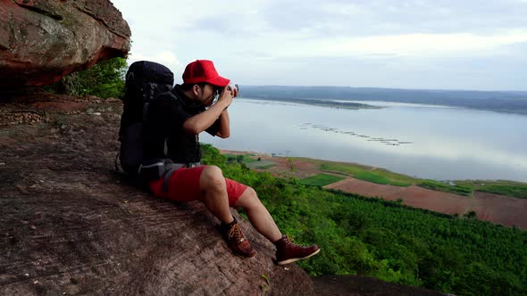 man traveler with backpack using camera taking a photo on the edge of cliff